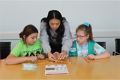  Graduate student works at a table with two girl scouts on a biomedical engineering project in Weill Hall.